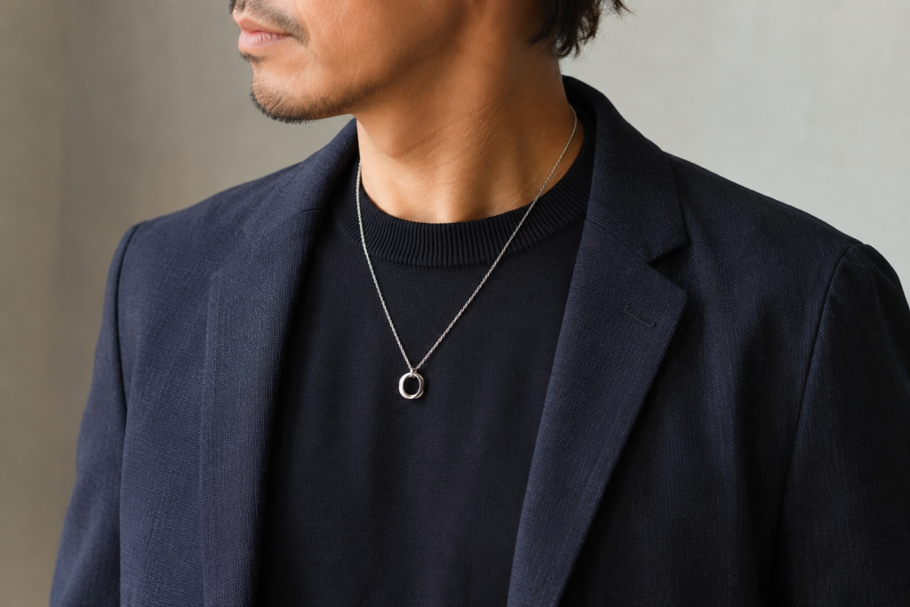 40代男性が黒ニットとネイビージャケットにリング型のシルバーネックレスを合わせた大人のコーディネート